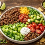 Healthy taco salad with ground beef romaine lettuce avocado tomatoes cheddar cheese salsa and sour cream in a bowl